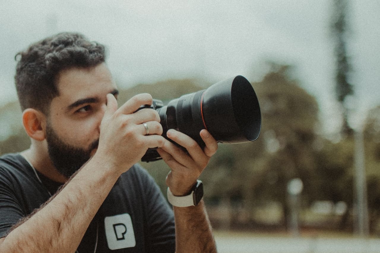 A focused photographer taking pictures outdoors with a Canon DSLR camera.