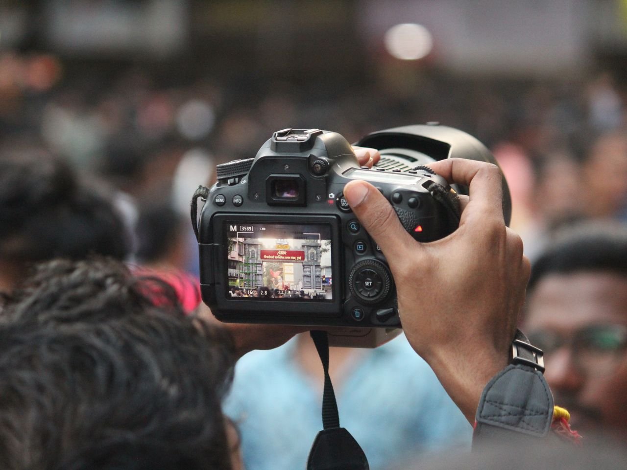 Hand holding a DSLR camera capturing a busy street scene in Mumbai, India.
