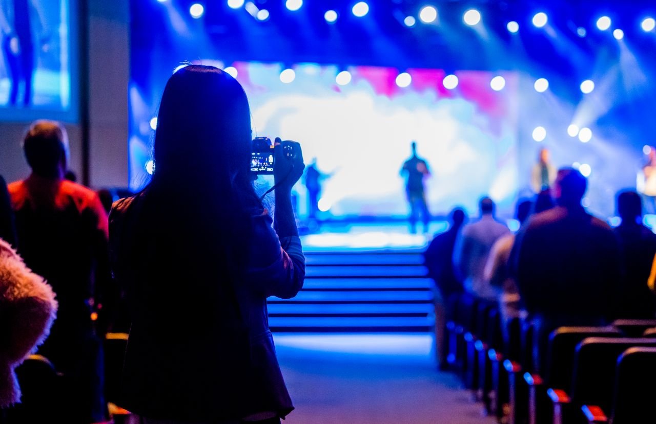 Audience capturing live concert moments with a smartphone from the back view.